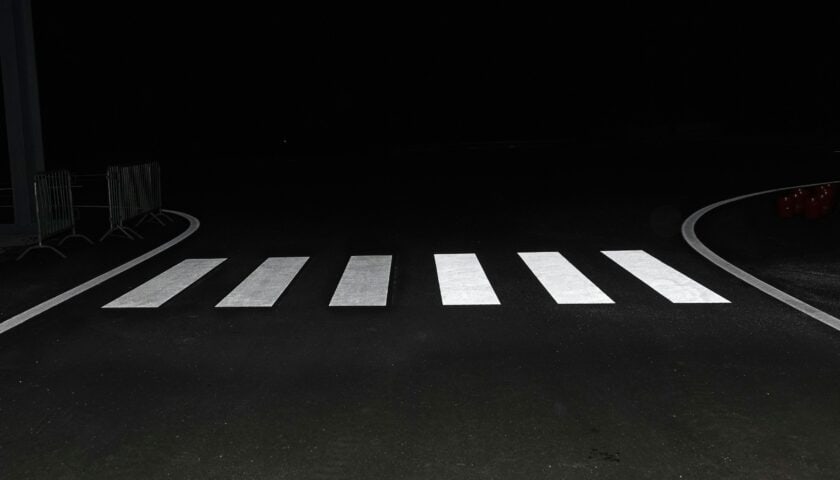 Bela horizontalna signalizacija pešačkog prelaza na tamnom kolovozu tokom noći.
